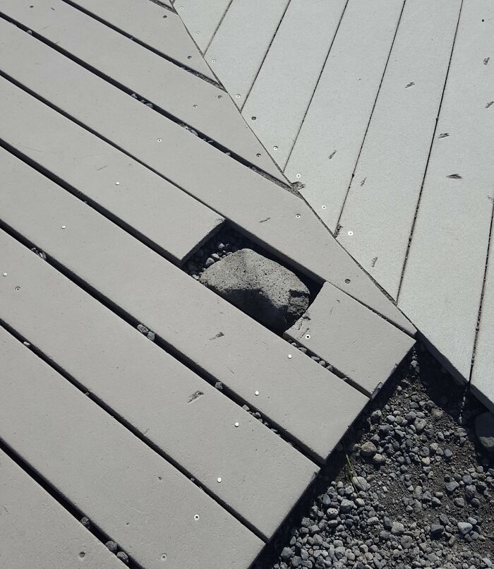 Uneven deck boards with a loose rock underneath, showing an imperfect outdoor surface that may annoy people with OCD.