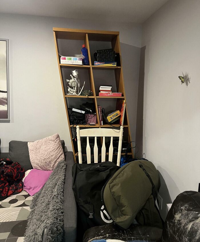 Leaned wooden shelf cluttered with items and bags blocking a white chair, showing imperfect things that annoy people with OCD.