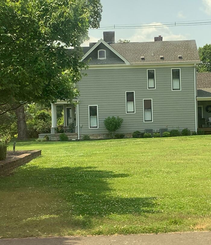 Gray house with misaligned windows and shutters surrounded by green lawn and trees, showing imperfect things for OCD viewers.