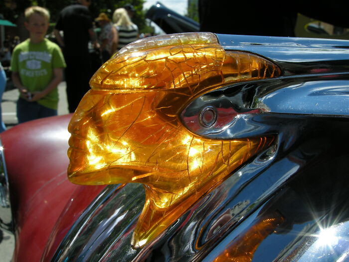 Close-up of a 1950s car hood ornament shaped like a golden translucent Native American figure shining in sunlight.
