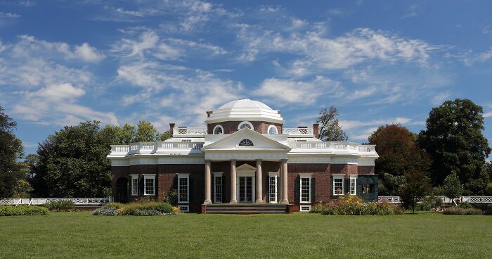 Historic home with classic American architecture featuring columns and a dome, set against a blue sky and green lawn.
