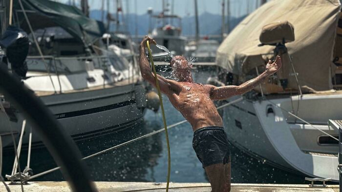 Man bathing with hose on a dock near boats, an accidental renaissance photo capturing natural light and motion.