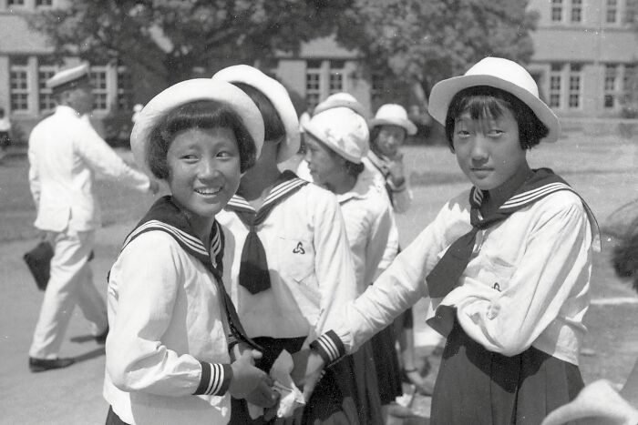 Japanese school children in uniform smiling and holding hands outdoors during World War II era schools worldwide.