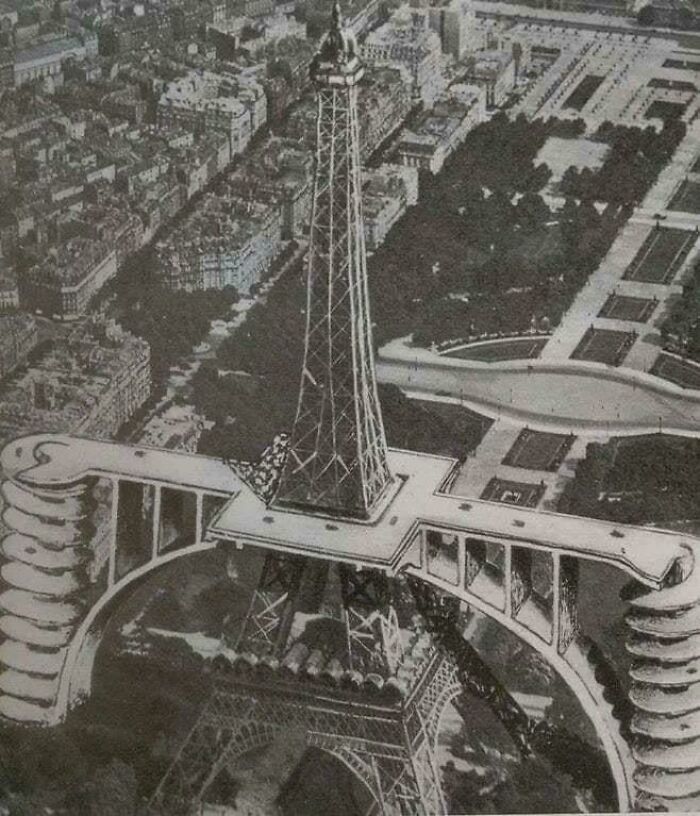 An old black and white photo shows the extremely large Eiffel Tower with an eerie, wide base structure extending horizontally.
