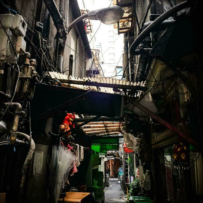 Narrow urban alley with cluttered pipes, wires, and makeshift roofs illustrating urban hell and societal decay.