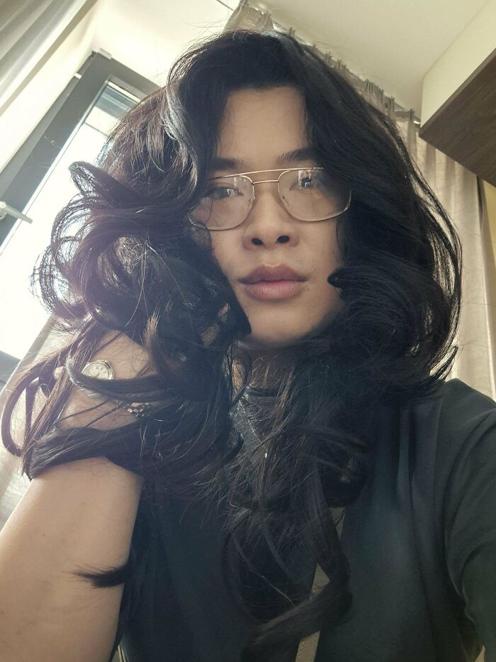 Man with fierceflow beautiful hair wearing glasses indoors by a window with natural light and dark clothing.