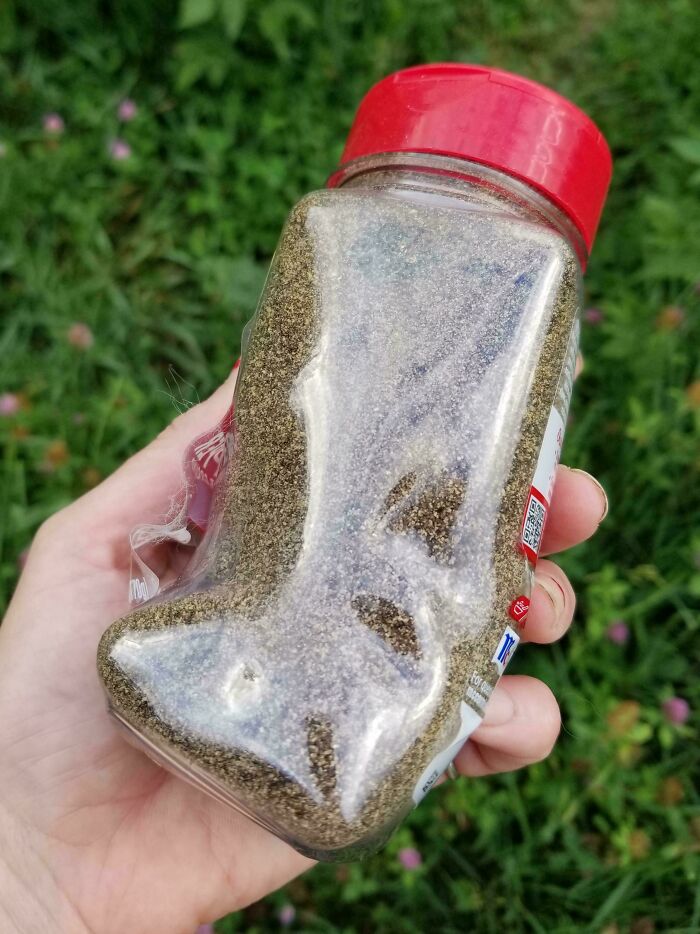 Hand holding a heatwave-melted plastic spice bottle distorted into a boot shape against a blurred grass background.