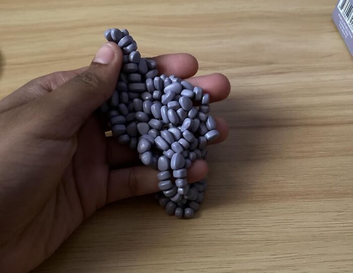 Hand holding dark purple beaded bracelet on wooden surface, showcasing peak coolness accessory to covet.