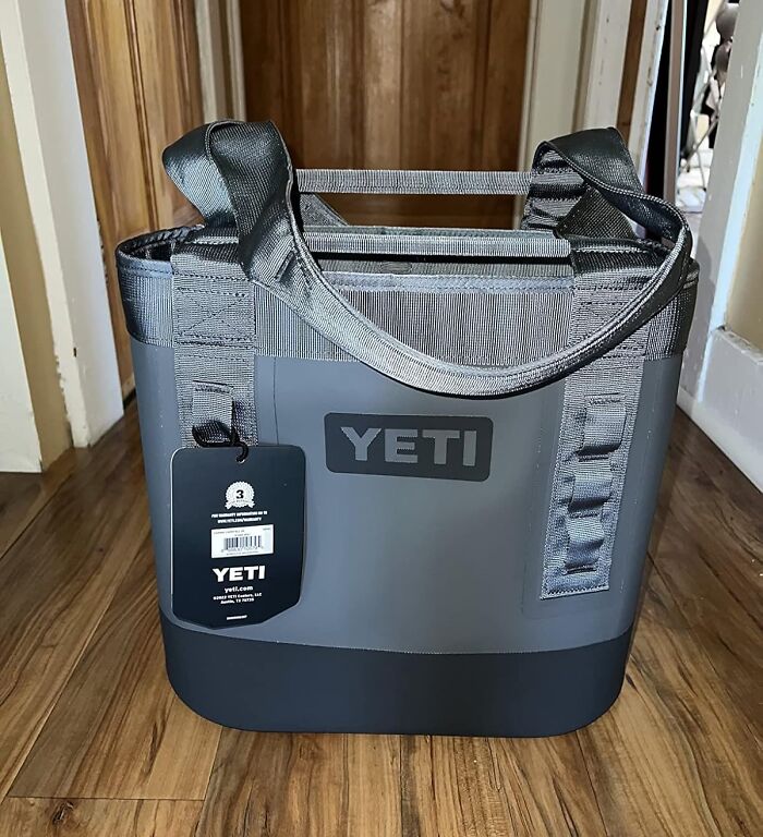 Gray YETI soft cooler bag with sturdy handles and a black tag, sitting on wooden floor indoors, peak coolness gear.
