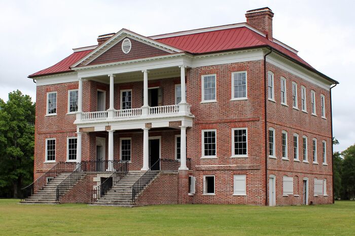Large historic brick home with white columns and red roof showcasing America’s architectural heritage.