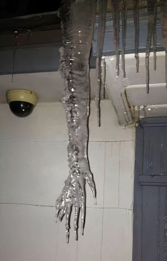 Long, eerie icicles hanging from a roof edge, resembling a frozen hand, a terrifying moment nature stopped people in their tracks.