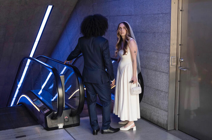 Couple in wedding attire at an escalator, captured in a funny accidental image by street photographer.