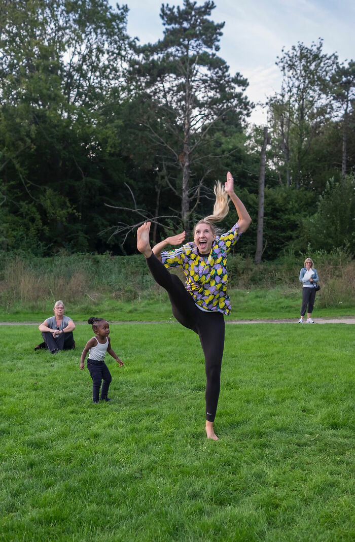 Woman in colorful shirt striking a high kick pose on grass, captured by funny accidental street photographer at the right time.