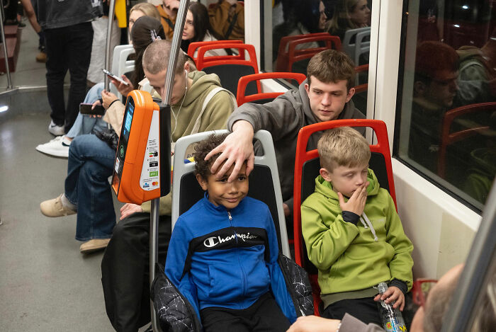Two boys sitting on a train, one smiling with a hand playfully on his head, captured by funny accidental street photography.
