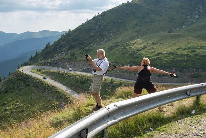 Two hikers accidentally create a funny scene while taking photos on a mountain road captured by street photographer.