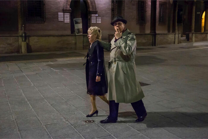 Couple walking at night in vintage style clothing, captured in a funny accidental moment by a street photographer.