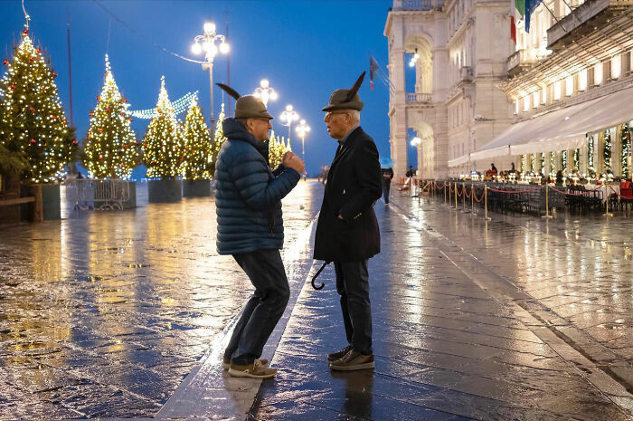 Two men wearing feathered hats, captured in a funny accidental image by a street photographer at night.