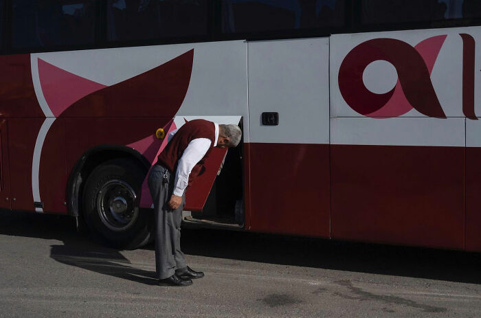 Man leaning into bus storage compartment creating funny accidental image taken at right time by street photographer.