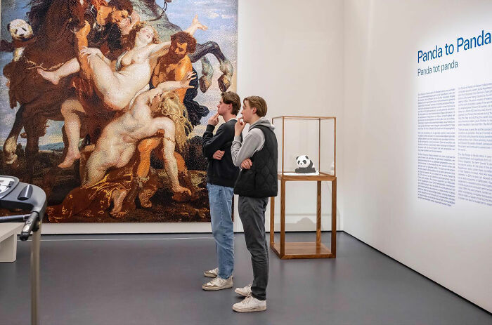 Two young men thoughtfully observing a large classical painting in an art gallery, showcasing street photography timing.