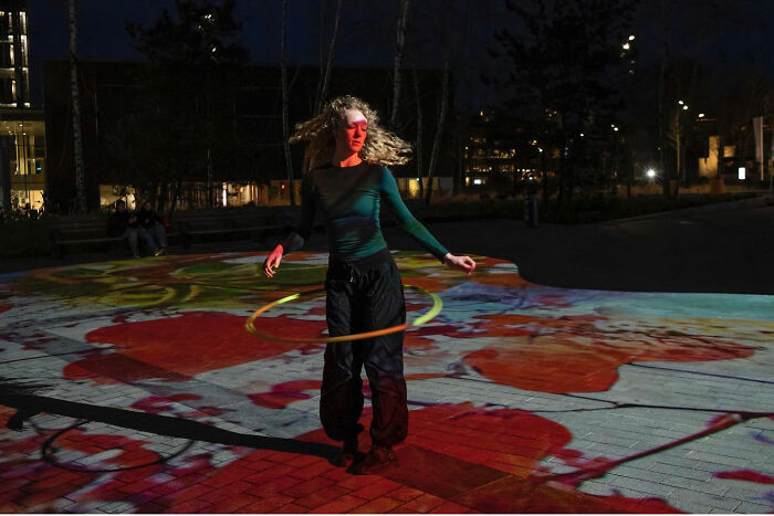 Woman with curly hair hula hooping at night outdoors, captured by street photographer’s funny accidental image.