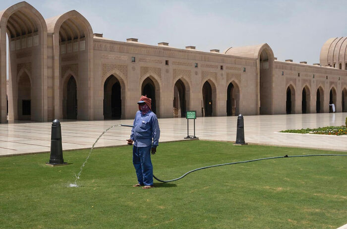 Man watering grass with hose forming a funny accidental image taken at the right time and place by street photographer