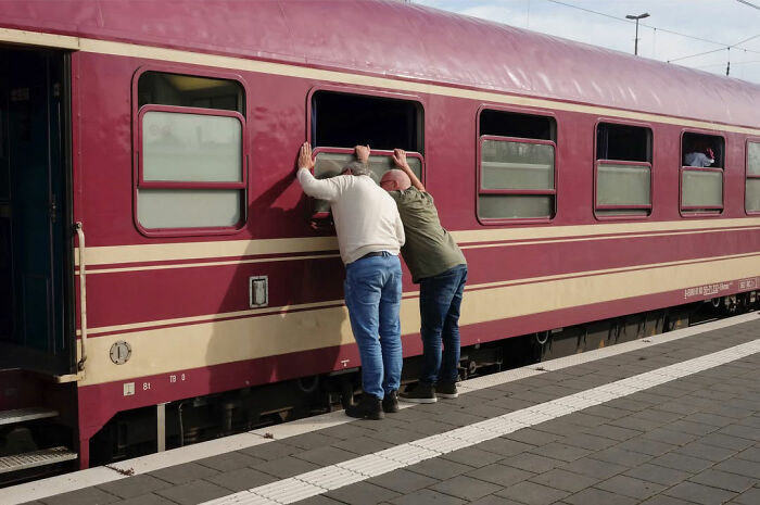 Two men leaning through a train window creating a funny accidental image captured by a street photographer.