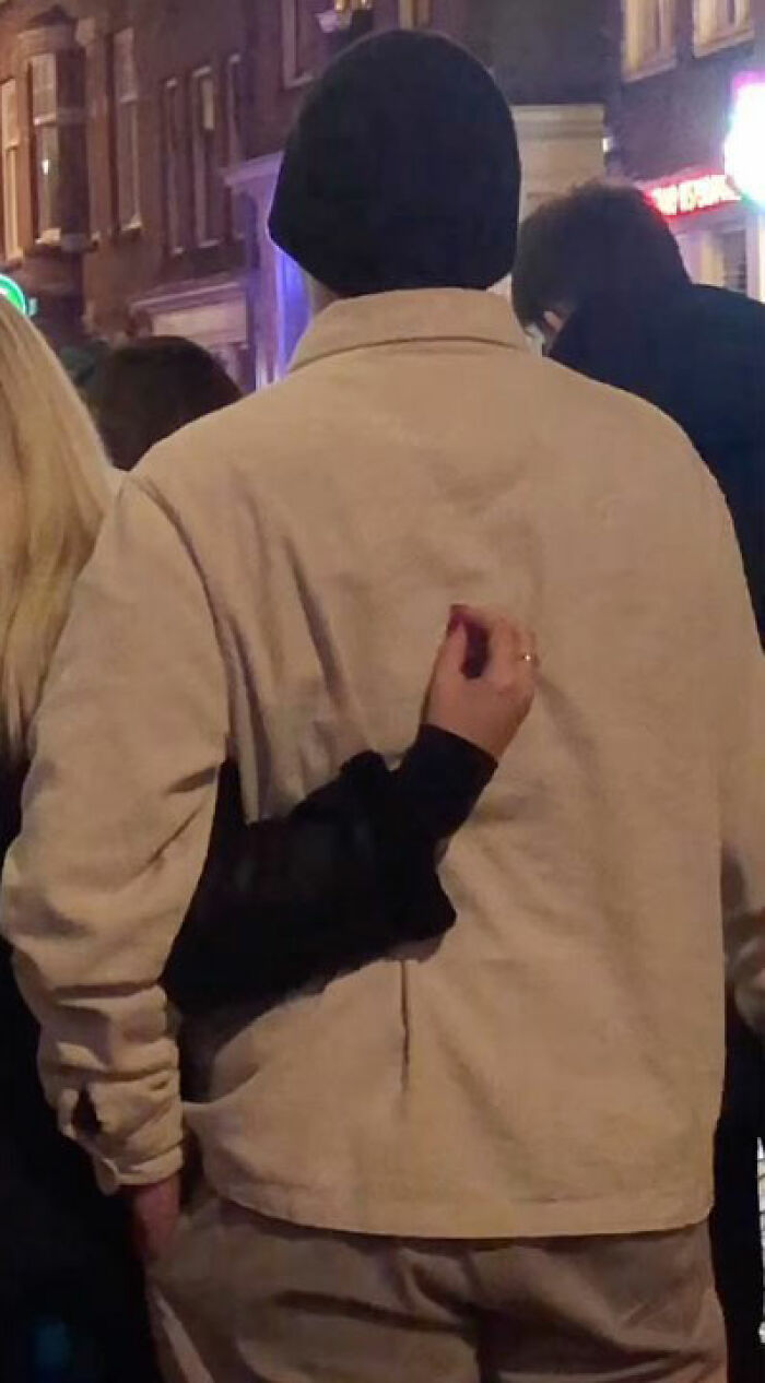 Accidental street photography captures a funny moment of a person appearing to have a tiny hand grabbing their back at night.