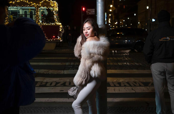 Woman in a fur coat posing on a city street at night, captured by a street photographer at the right time and place.