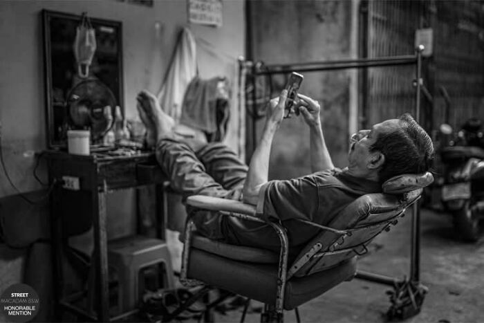 Man reclining in a chair, using a phone in a black and white street photo capturing daily life moments.