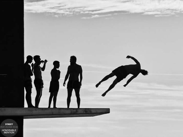 Black and white street photo of five people on a diving board, one mid-air jump, capturing dynamic movement and contrast.