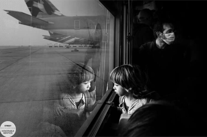 Black and white street photo of a child looking out a window with reflections, capturing a reflective moment.