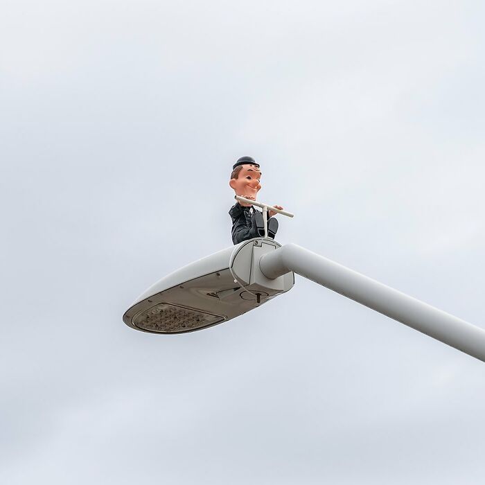 Street art featuring a character playing a flute atop a modern street lamp, showcasing public space creativity by Frankey.