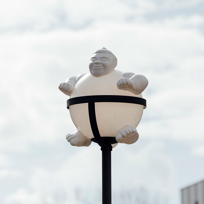 Street art of a sumo wrestler figure creatively integrated into a public space lamp post design by Frankey.