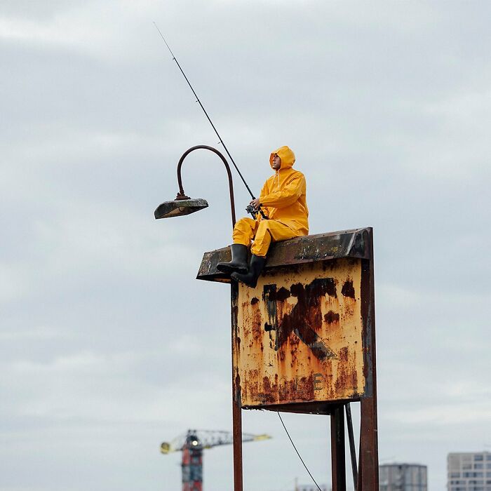 Street art installation by Frankey showing a person in yellow rain gear fishing from a rusty urban structure.