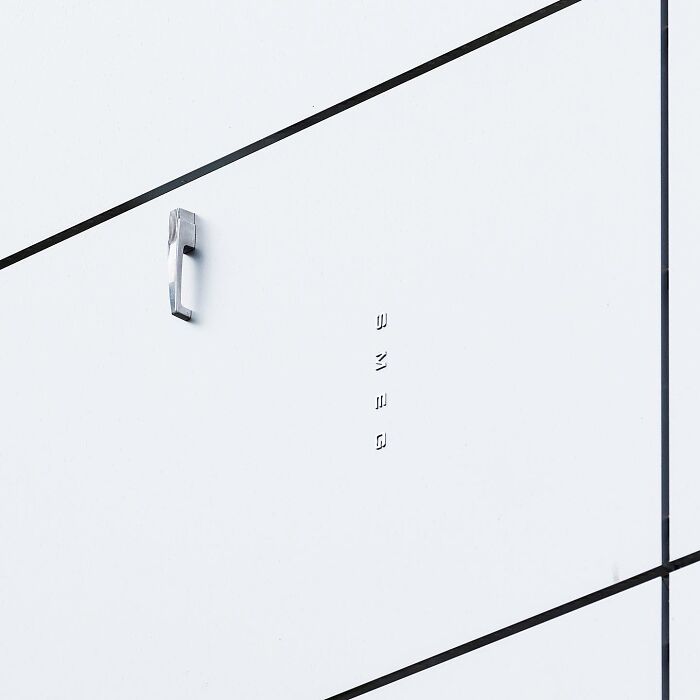 Minimalist public space featuring clever street art with a metal phone handset mounted on a white wall panel.