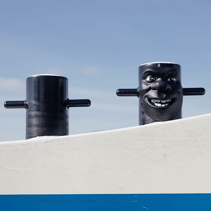 Black street art bollard with a smiling face creatively transforming public spaces through clever street art by Frankey.
