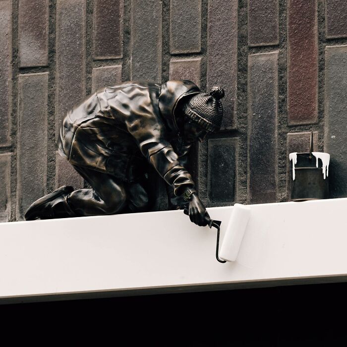 Street art sculpture of a person painting a white surface, showcasing clever interpretations of public spaces.