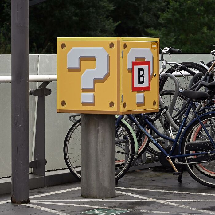 Yellow street art box with question marks near parked bicycles, a clever interpretation of public spaces through street art.