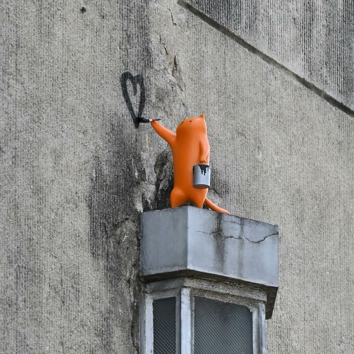 Orange cat figure painting a heart shape on a textured wall, showcasing clever street art in public spaces by Frankey.
