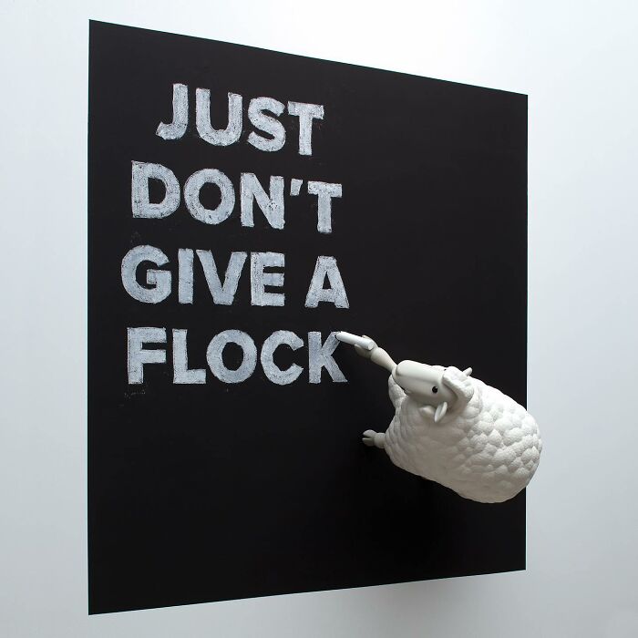 Street art with a 3D sheep sculpture interacting with a blackboard featuring bold white text in a public space.