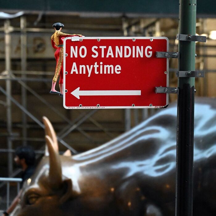 Miniature street art figure climbing a no standing sign, showcasing clever interpretations of public spaces through street art.
