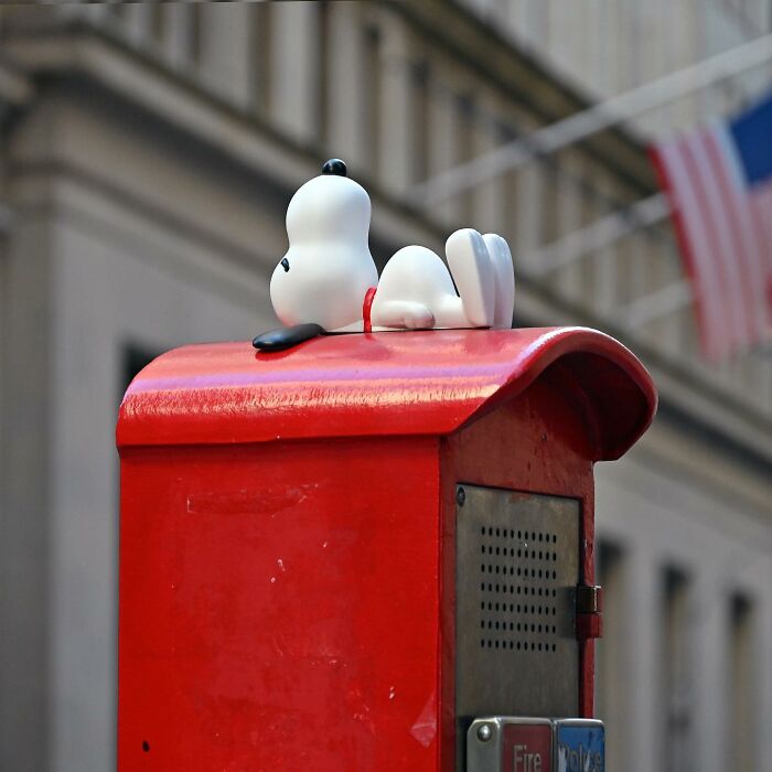 Snoopy figure lying on top of a red fire alarm box as clever street art in a public space.