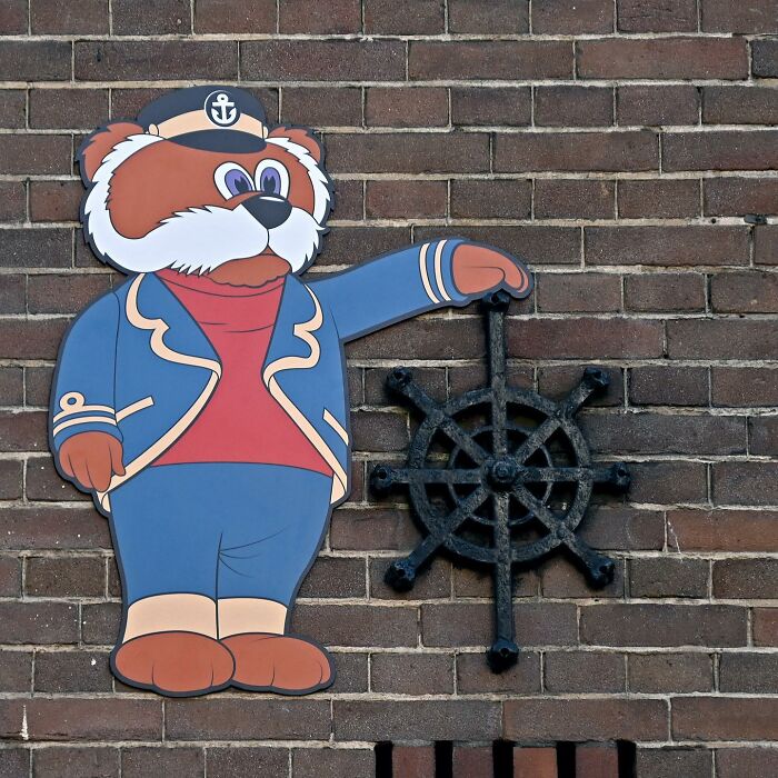 Street art by Frankey featuring a cartoon sailor bear interacting with a ship's steering wheel on a brick wall.