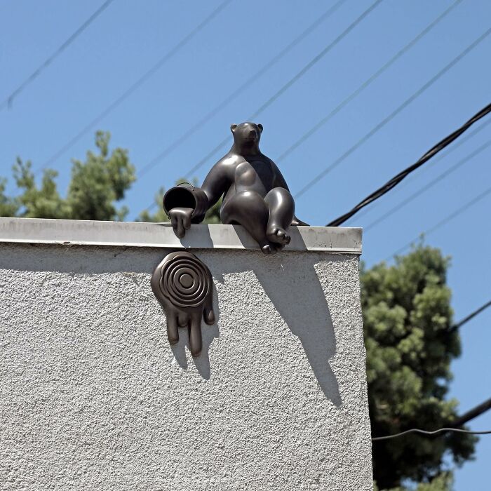 Sculptural street art of a bear pouring liquid from a tilted cup, creatively transforming public spaces with clever design.