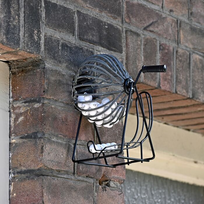 Metal street art of a bingo cage with balls attached to a brick wall, showcasing clever public space interpretation.