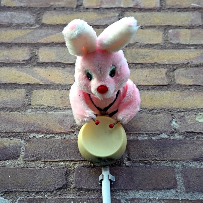 Pink plush bunny attached to a brick wall playing street art drums, showcasing clever interpretations of public spaces.