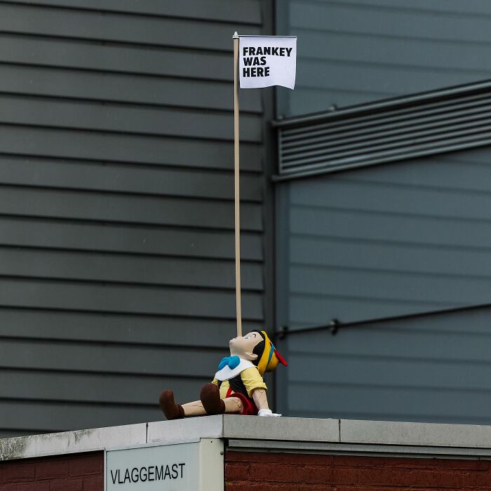 Pinocchio figure holding a flag with street art by Frankey on an urban rooftop, showcasing clever public space art.