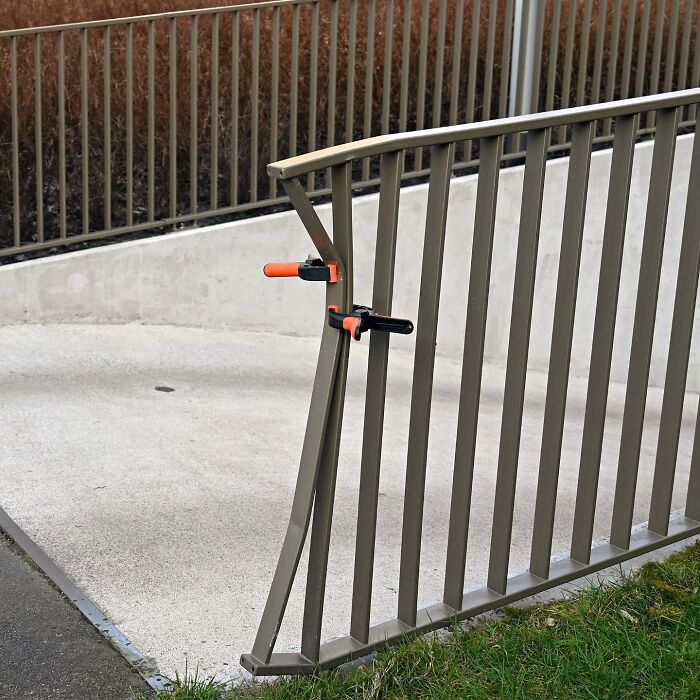 Bent metal railing clamped with orange and black clamps in a clever street art interpretation of public spaces.