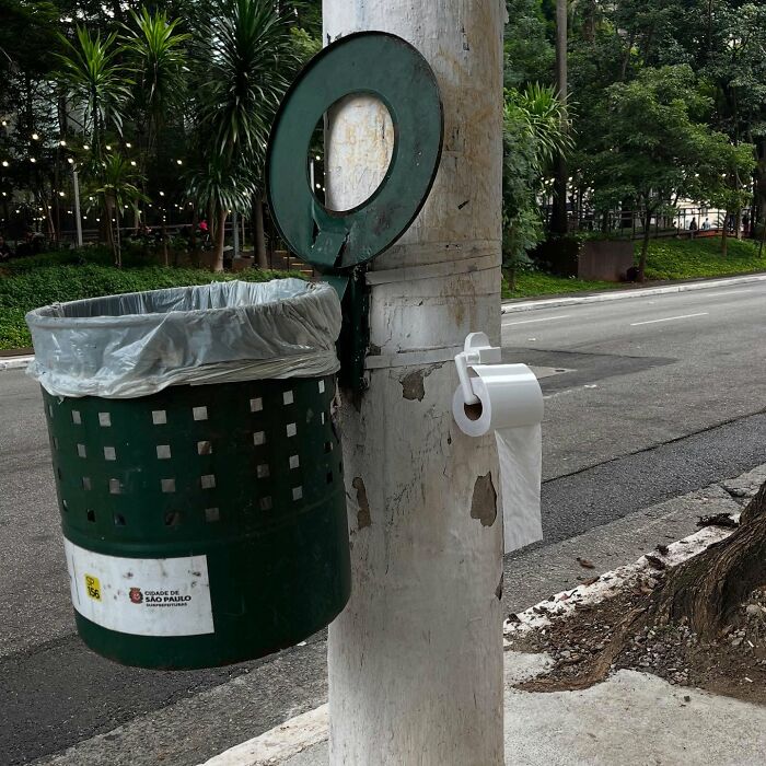 Street art cleverly integrated with public space featuring a trash bin and toilet paper roll on a city street.