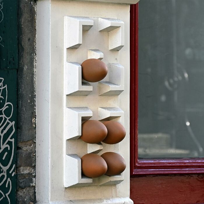 Street art installation featuring realistic eggs integrated into public space architectural detail.